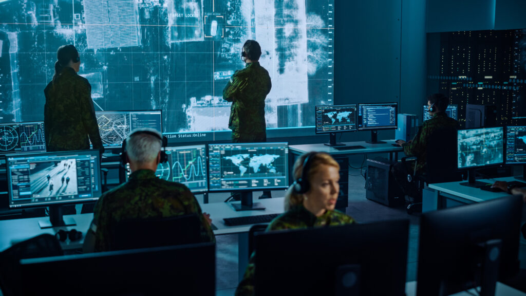 Military Surveillance Team Of Officers Locked A Target On A Vehicle From A Satellite And Monitor It On A Big Display In Office For Cyber Operations For Managing Security And Army Communications.